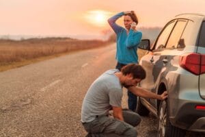 Male and female standing outside of car looking at the tire
